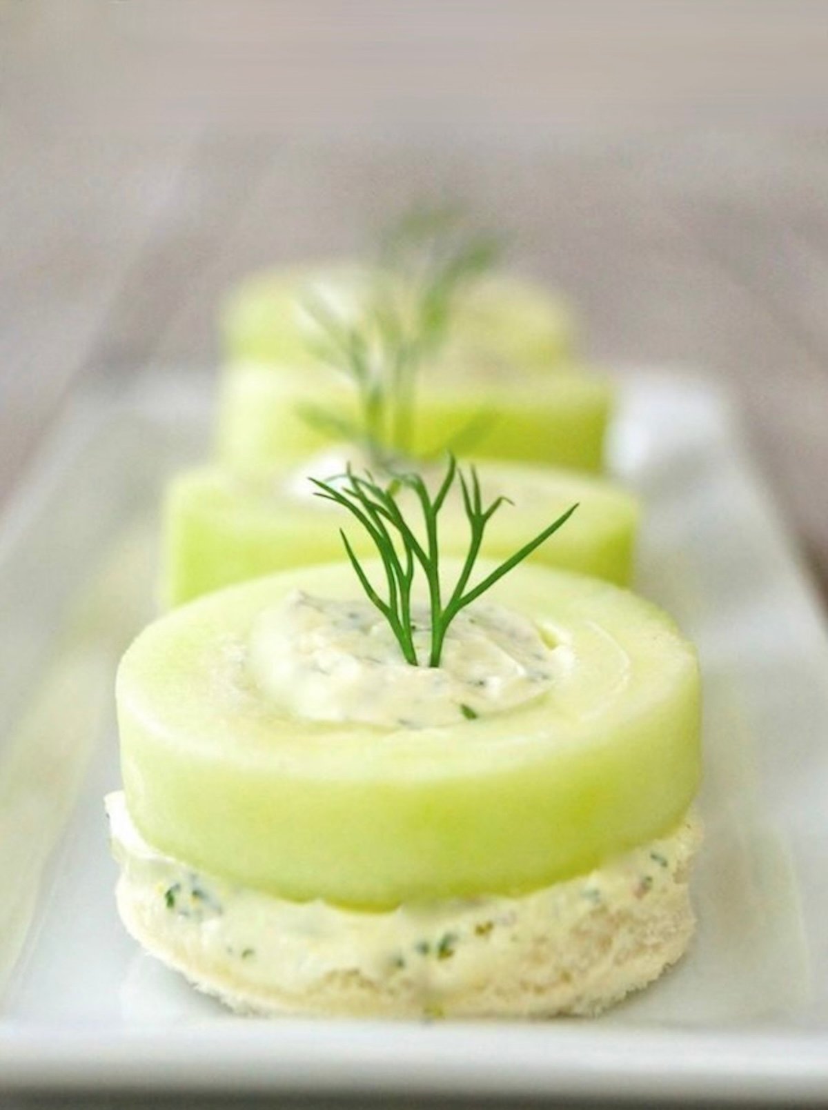 4 cucumber dill canapés on a narrow white dish.