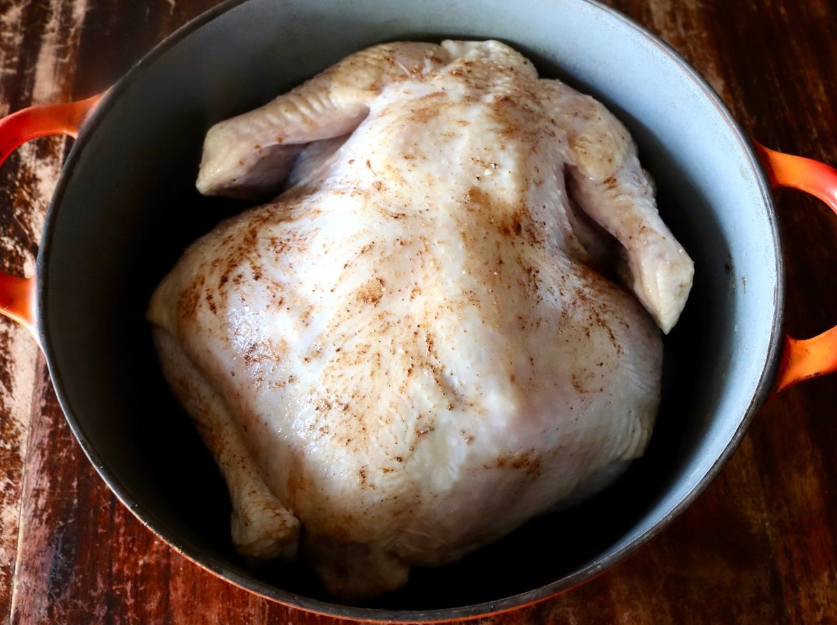 Whole raw chicken, breast side down, in a Dutch Oven with spices on top.