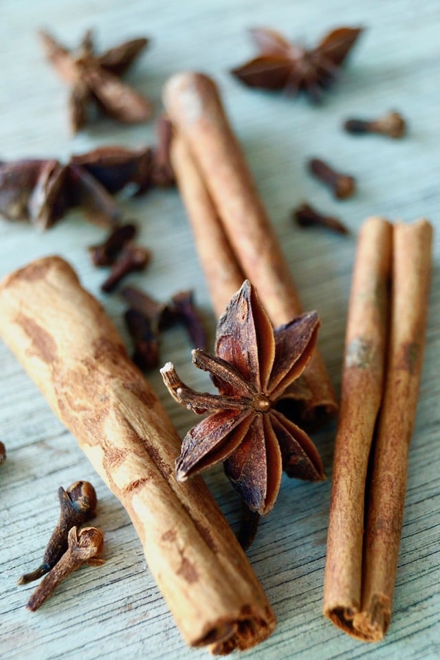 Whole spices including cinnamon sticks, star anise and cloves, on a llight green wood board.