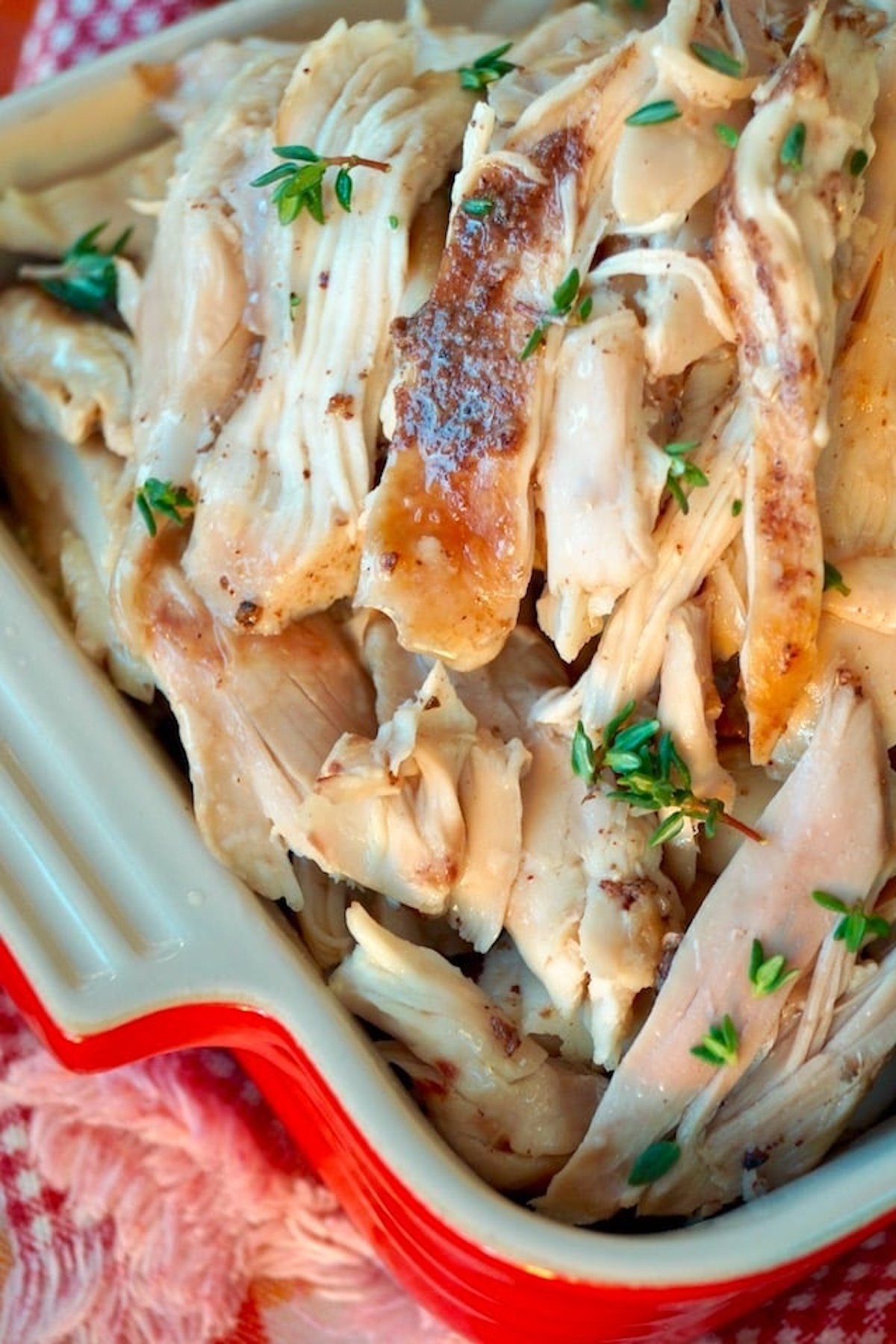 Close up of shredded Fall-Apart Dutch-Oven Chicken in a small square casserole dish on a red-checked cloth.