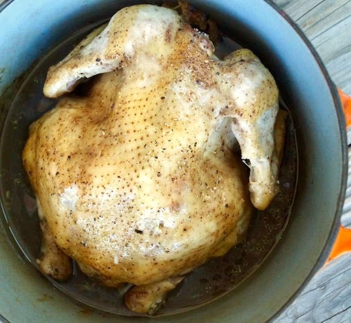 Whole cooked chicken, breast side down, in a Dutch Oven with spices on top.