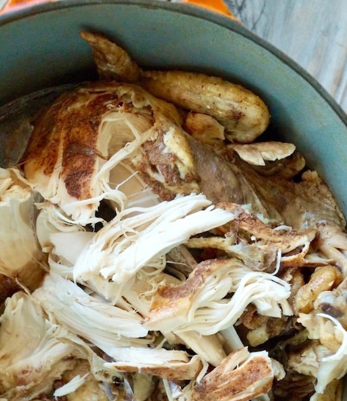 Close up of shredded chicken with bones in Dutch oven.