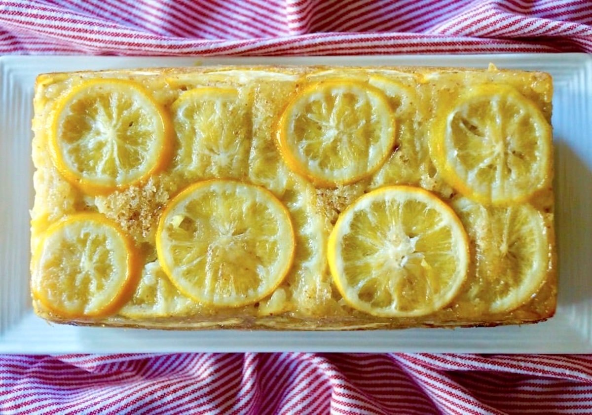 Lemon Loaf Cake with Olive Oil on white platter with red cloth beneath it.