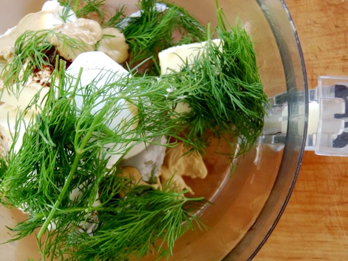 Food processor bowl filled with fresh dill, butter, cream cheese and mustard.