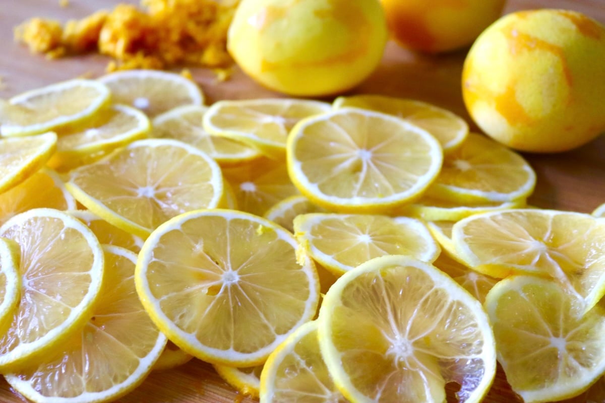 Cutting board full of very thinly sliced lemons, a couple of zested lemons and a pile of lemon zest.