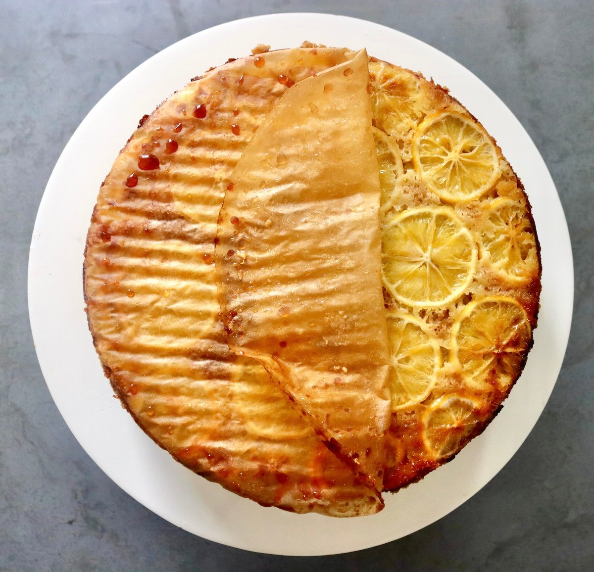 Inverted Lemon Cake with Parchment paper being peeled off the top to reveal lemon slices.