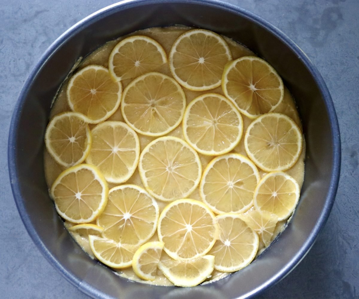 Lemon slices on top of batter in a cake pan.