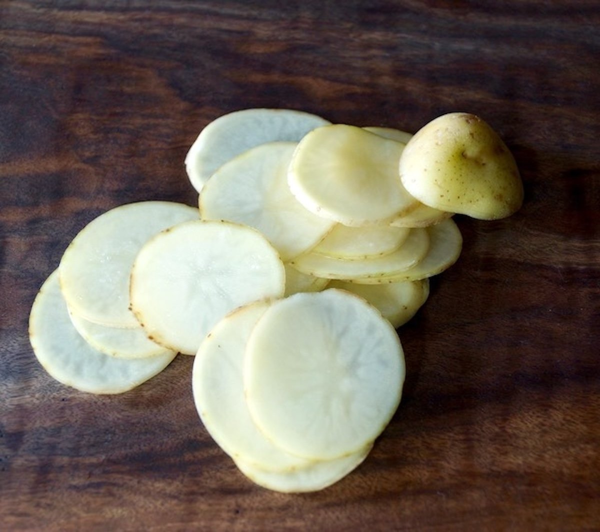 Thinly sliced potato rounds on a dark wood cutting board.