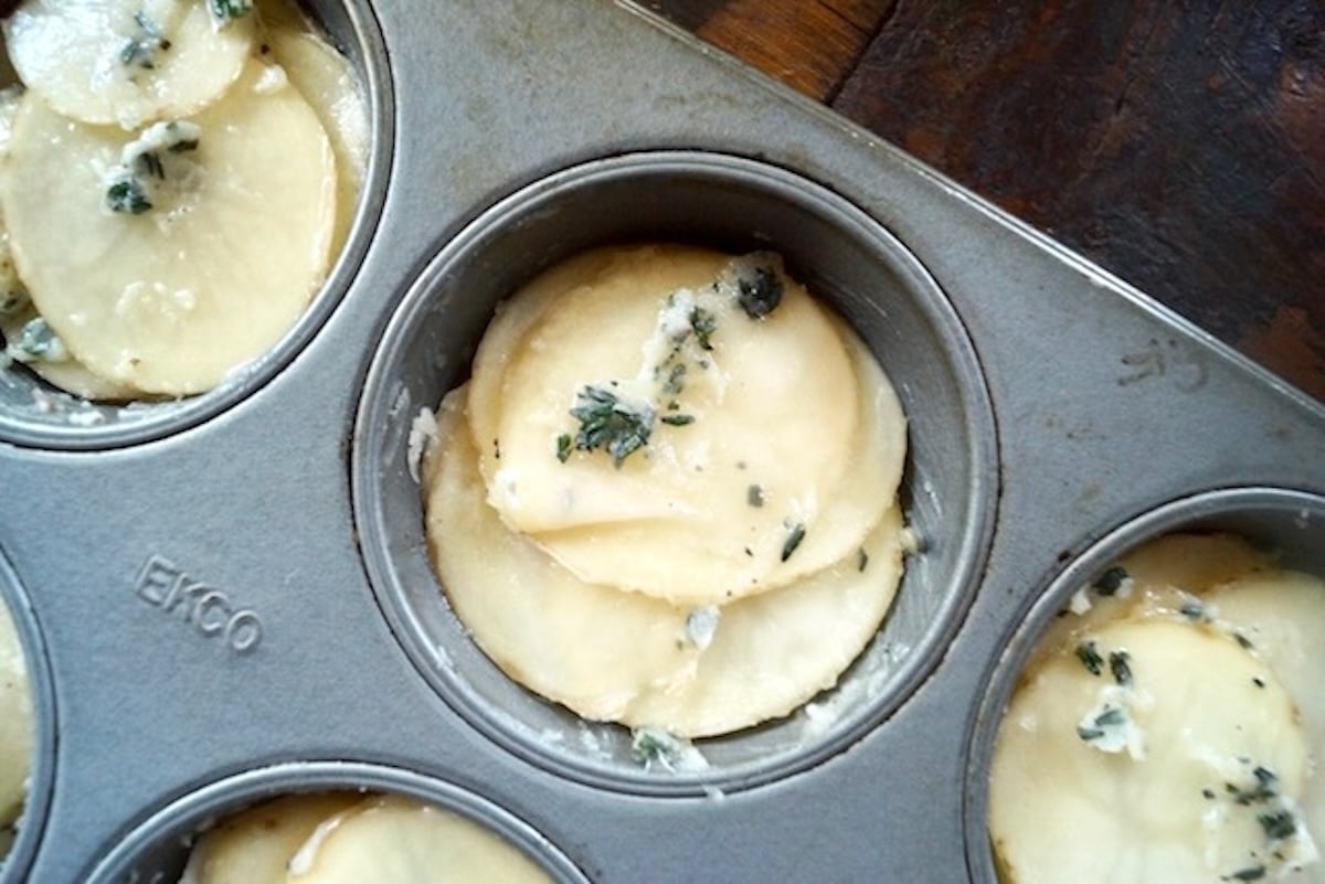 Muffin tin with thinly sliced potatoes in each cup.