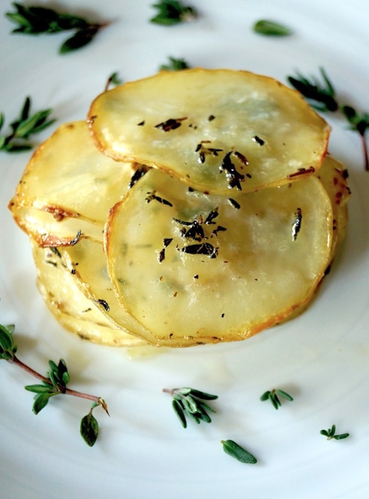A single-serving Pommes Anna in the middle of a white plate surrounded by thyme sprigs.
