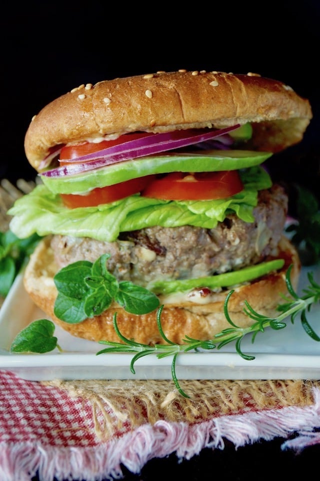 Grilled Mediterranean Burger in a bun with all the fixins on a small, white, square plate.