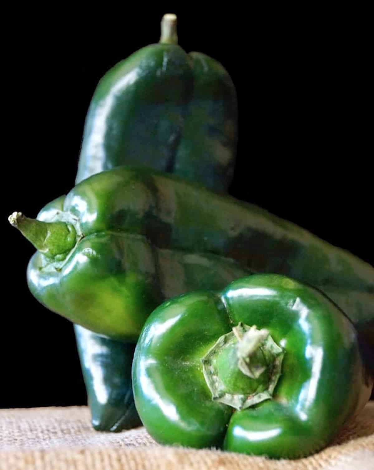 3 raw poblano chiles with a dark background.
