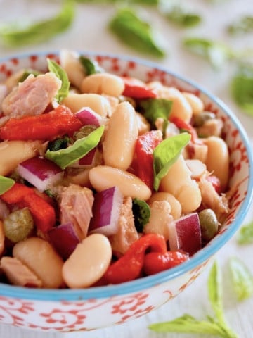Cannelllini Bean Tuan Salad i a white bowl with blue trim and red flowers on it.