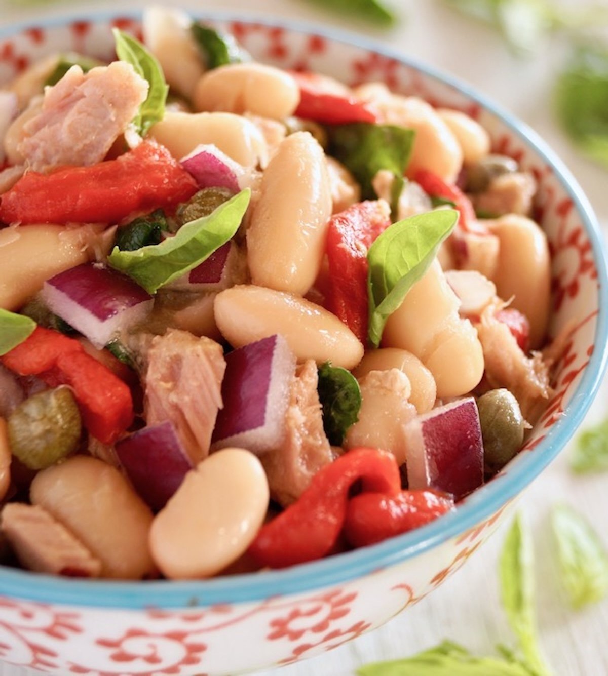 Cannelllini Bean Tuan Salad i a white bowl with blue trim and red flowers on it.