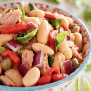 Cannelllini Bean Tuan Salad i a white bowl with blue trim and red flowers on it.