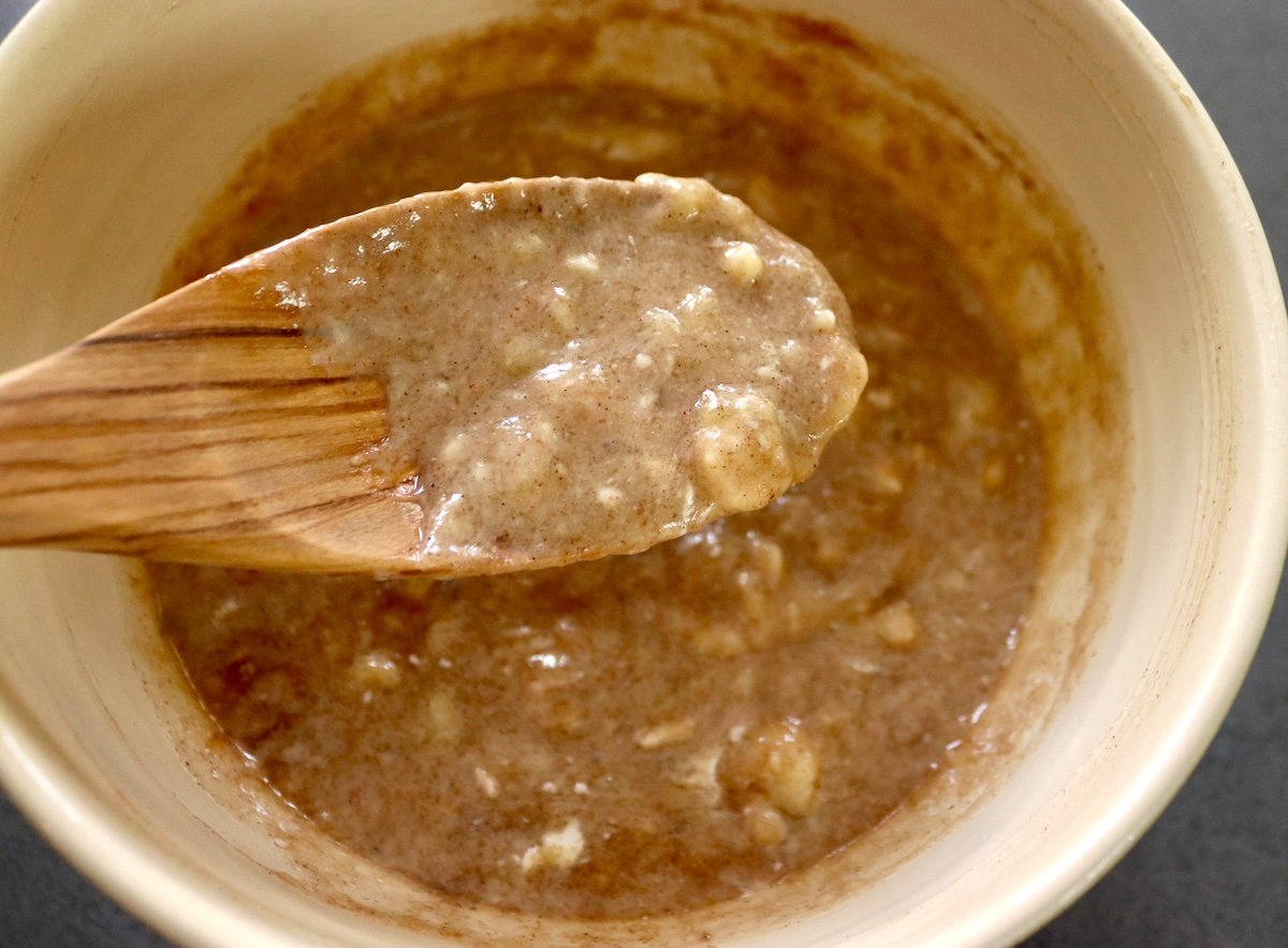 Gluten-free banana cake batter halfway made with wooden spoon holding some of it out of the bowl.