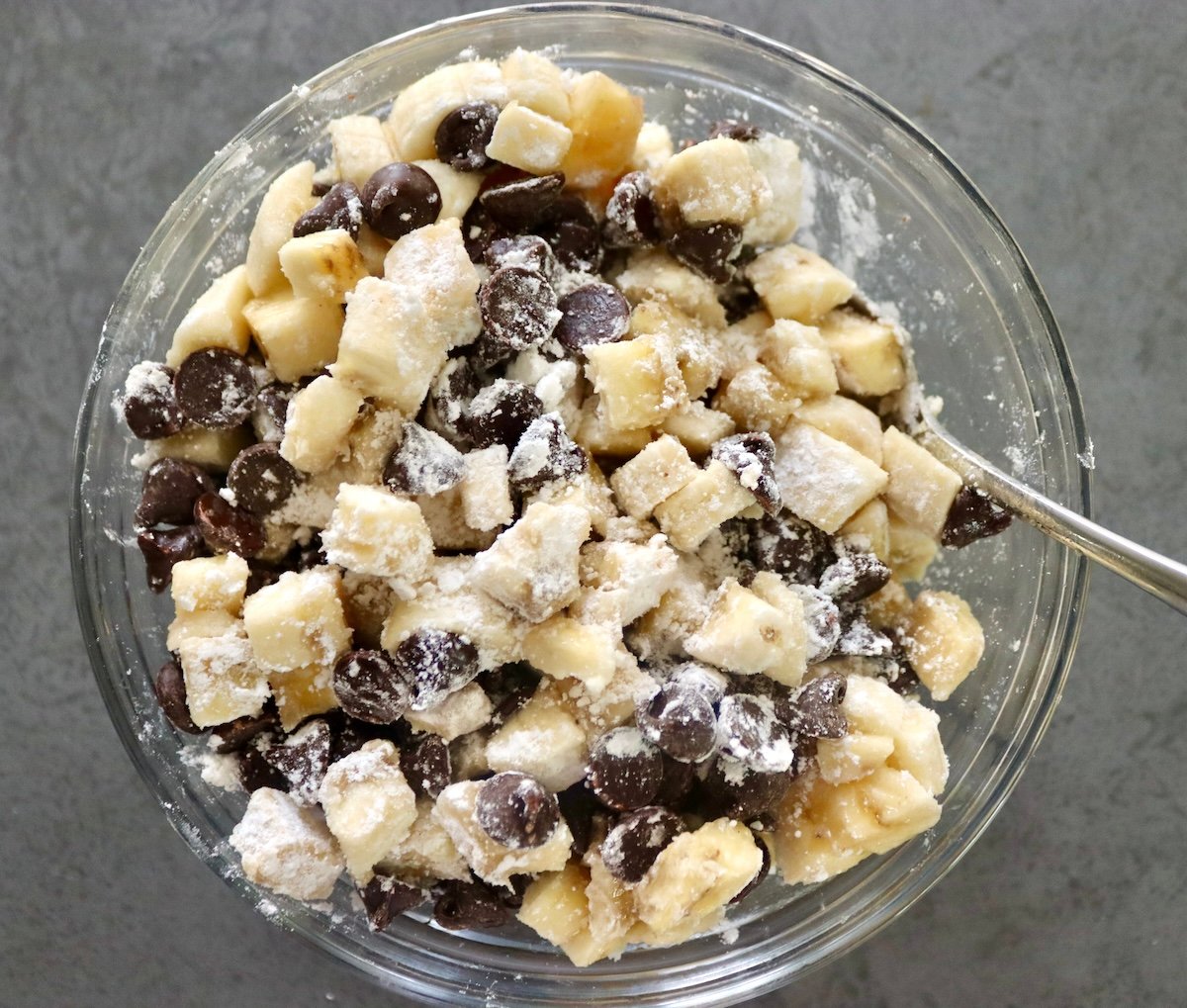 Small glass bowl filled with flour mixed with chocolate chips and diced banana.
