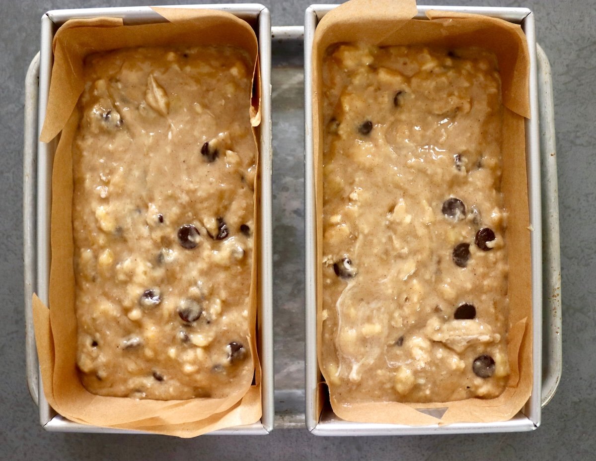 Two loaf pans lined with parchment paper and filled with gluten-free chocolate chip banana cake.