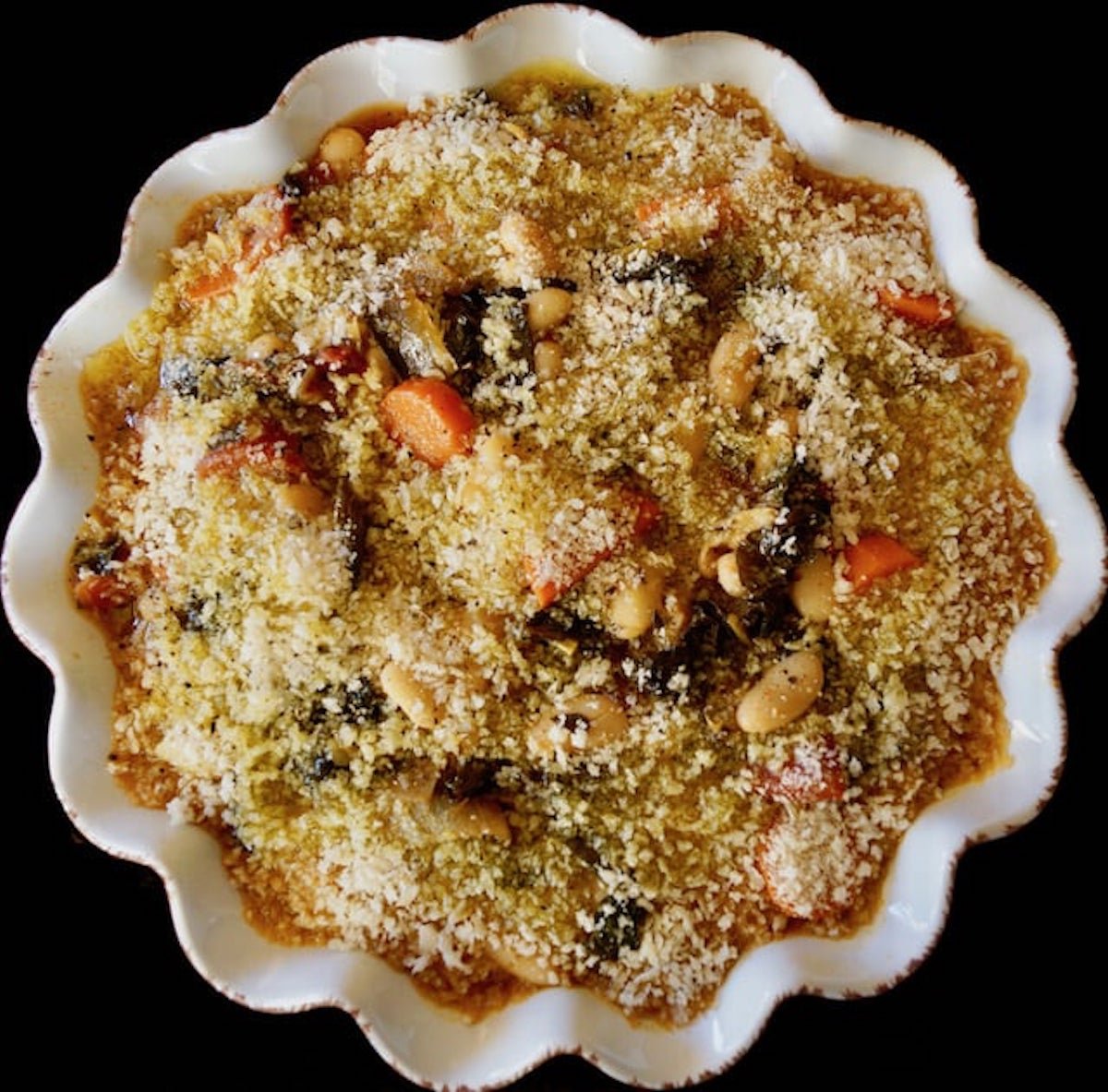 Crimped white pie plate filled with white beans, carrots, tomato and kale, topped with rbead crumbs for vegetarian .cassoulet