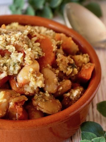 Small round terra cotta ramekin filled with vegetarian cassoulet with breadcrumbs on top.