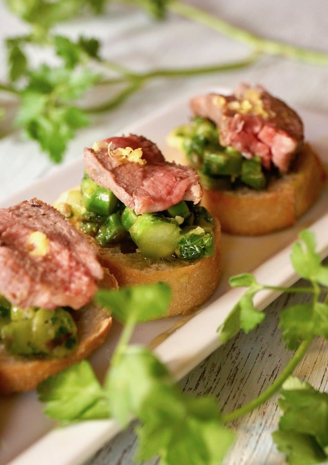 Three Asparagus Aussie Lamb Crostini on a white plate with fresh parsley.