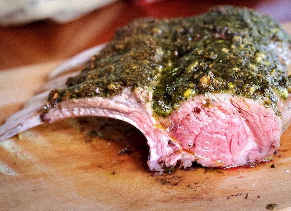 Rack of lamb crusted with pistachio and mint pesto, on wood board.