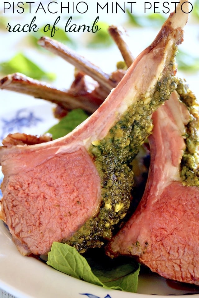 Several pesto-crusted lamb chops on a white plate with fresh mint leaves.