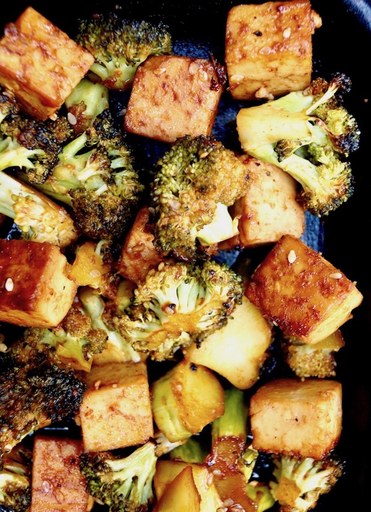 Roasted cubed tofu and broccoli pieces with sriracha honey sauce on sheet pan.