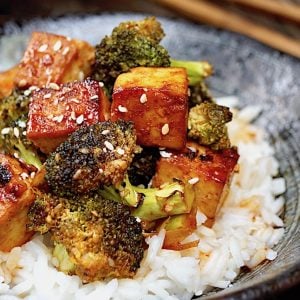 Sesame Sriracha Honey Tofu Broccoli in a black bowl with wooden chopsticks.