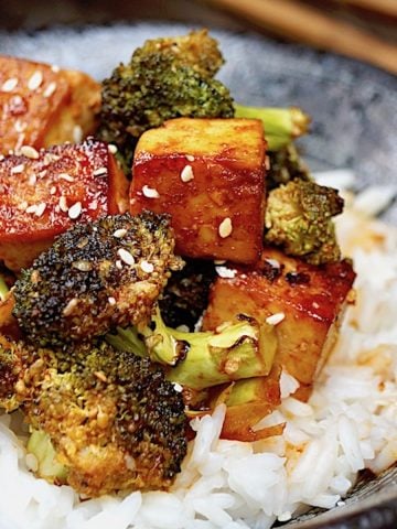 Sesame Sriracha Honey Tofu Broccoli in a black bowl with wooden chopsticks.