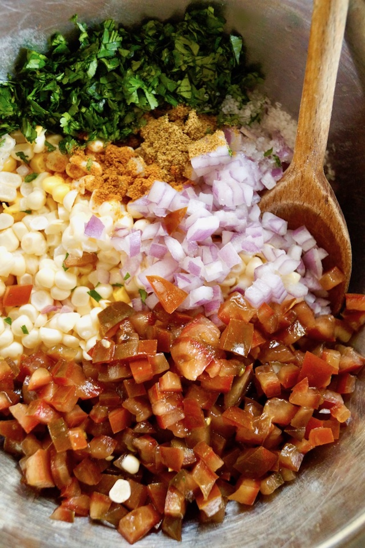 Sheet-Pan-Chipotle-Chicken-with-Corn-Salsa Finely chopped red onion, tomatoes and cilantro, with fresh kernels of corn in a bowl with a wooden spoon.