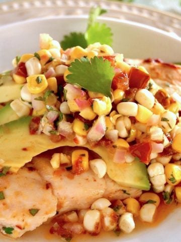 Sheet Pan Chipotle Chicken with Corn Salsa on a white plate with avocado and cilantro sprigs