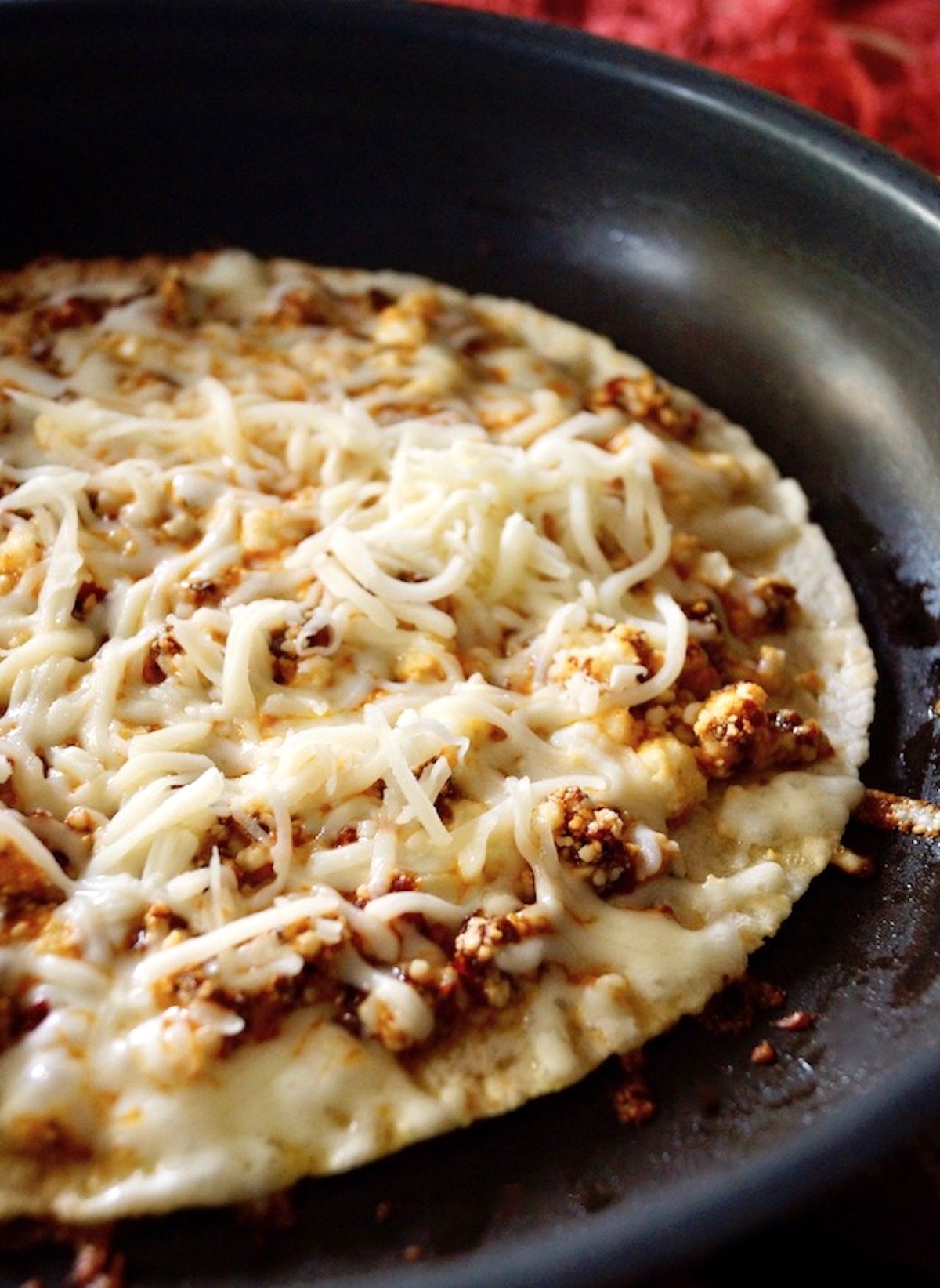 Tortilla in a pan with crumbled cheese mixed with red chili and mozzarella on top.