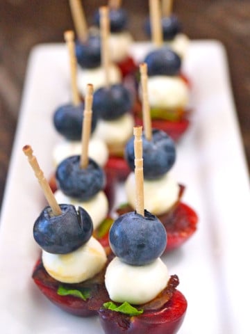 Several fruit appetizers on toothpicks with cherries and blueberries on a white plate.