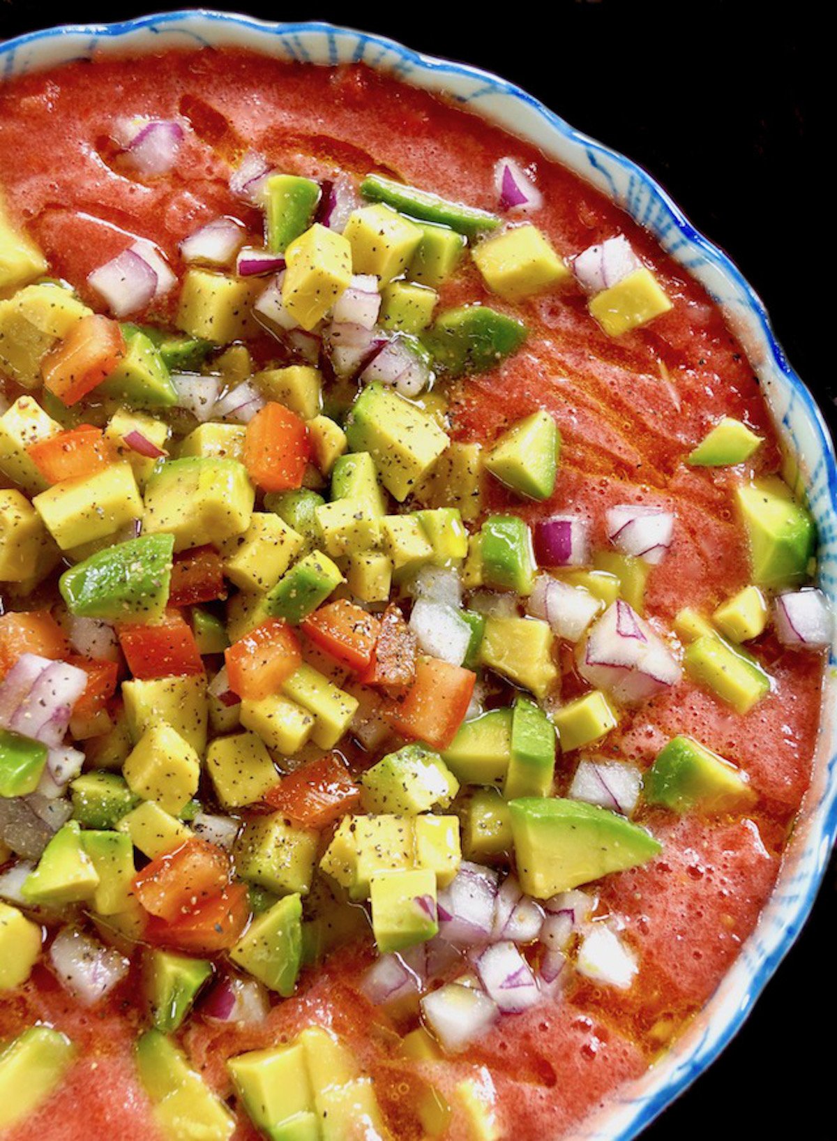 Top view of tomato gazpacho with tons of toppings including avocado, tomato and red onion.