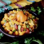 Black bowl filled with mango salsa with a small Habanero pepper right on top.