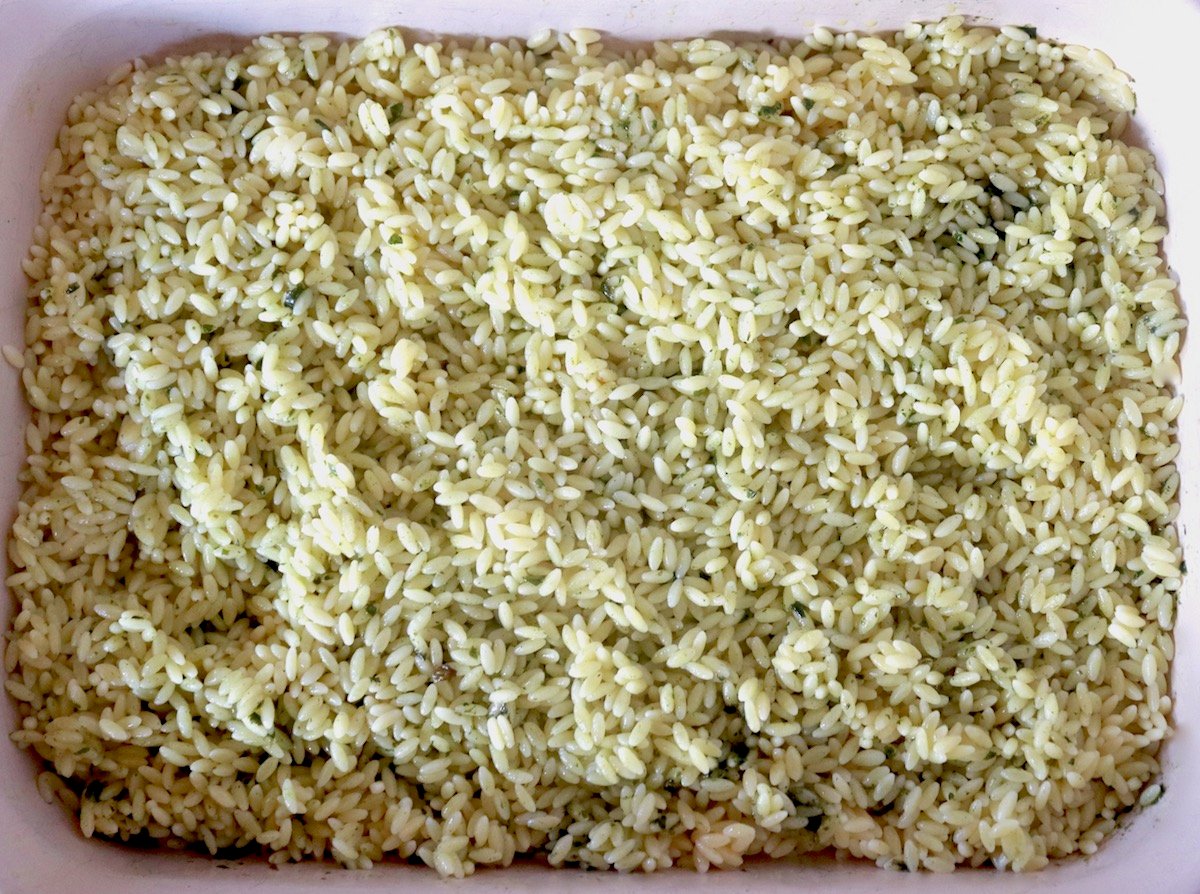 Orzo mixed with bits of basil spread on the bottom of a baking dish.