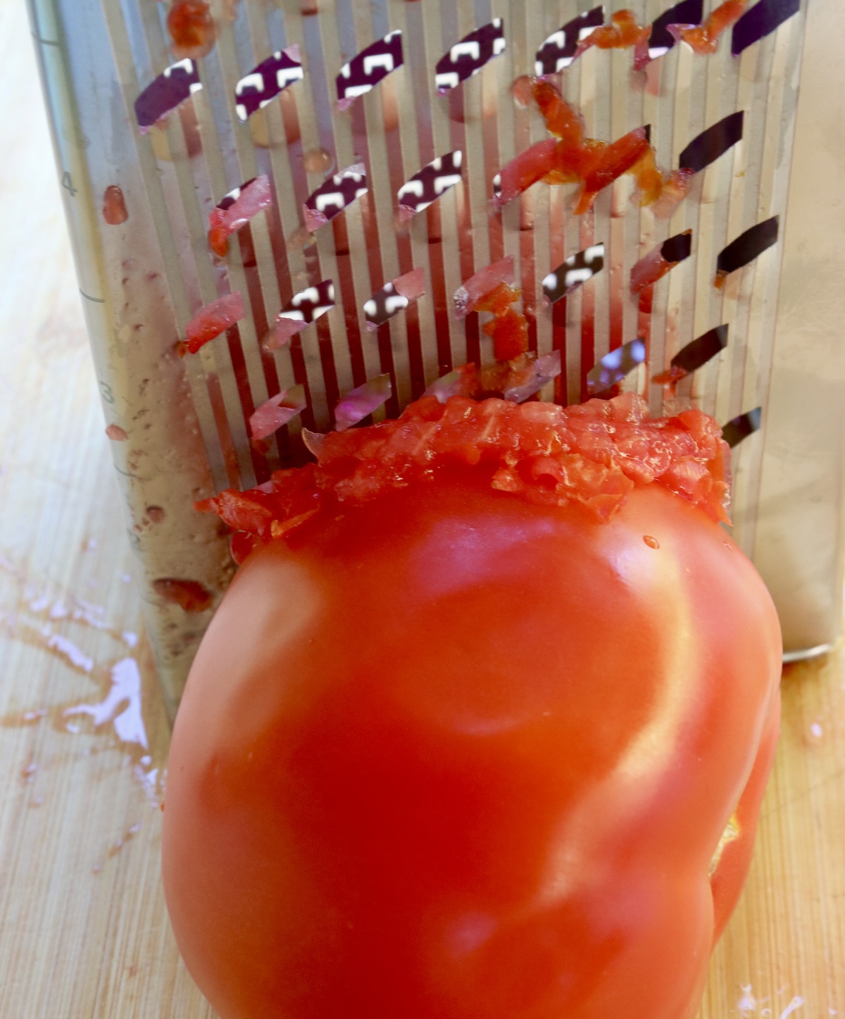 Sweet-Breakfast-Grated-Tomatoes-with-Olive-Oil Big beefsteak tomato being grated on a hand grater.