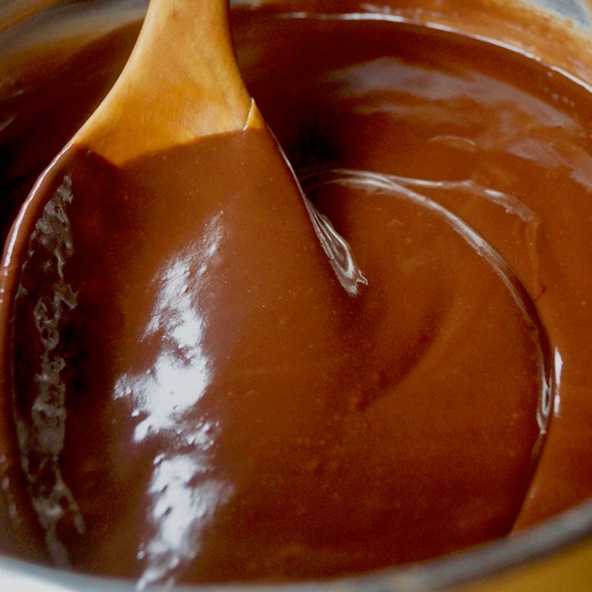 Chocolate ganache in a bowl with a wooden spoon.