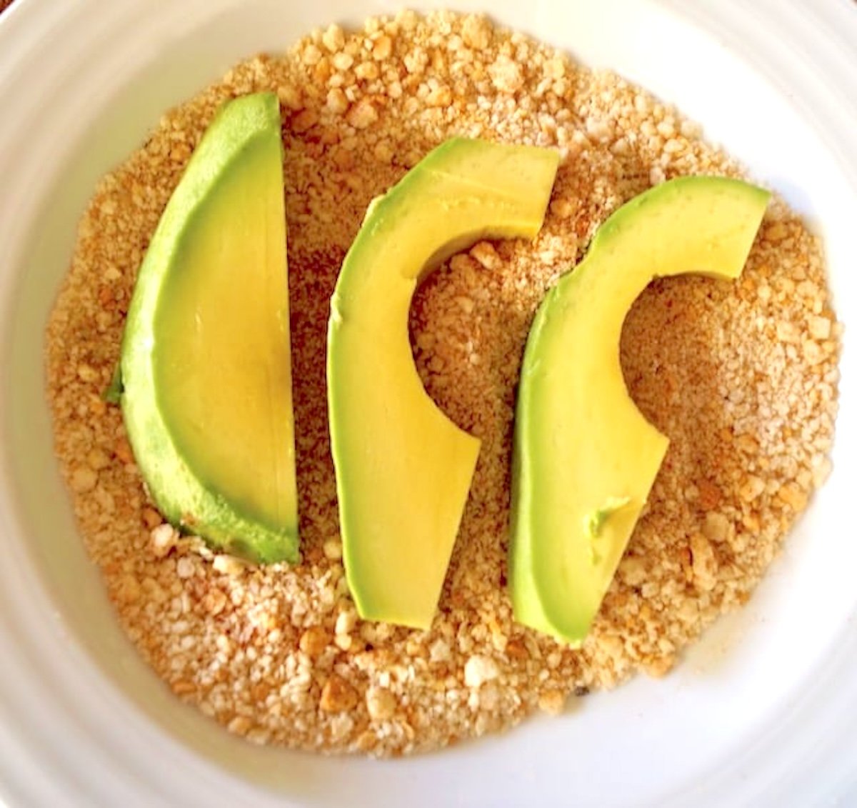 Avocado-Fries Turee slices of avocado on top of bread crumbs in a whilte bowl.