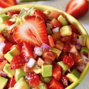 Light green bowl filled with strawberry and avocado salsa, with a halved strawberry on top.