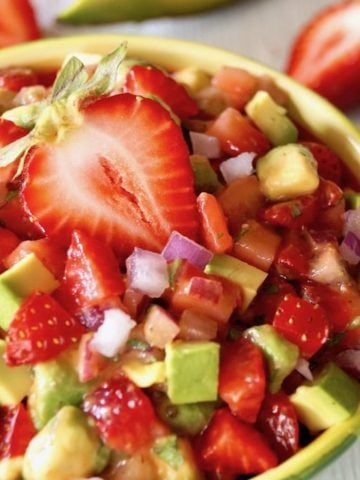Light green bowl filled with strawberry and avocado salsa, with a halved strawberry on top.