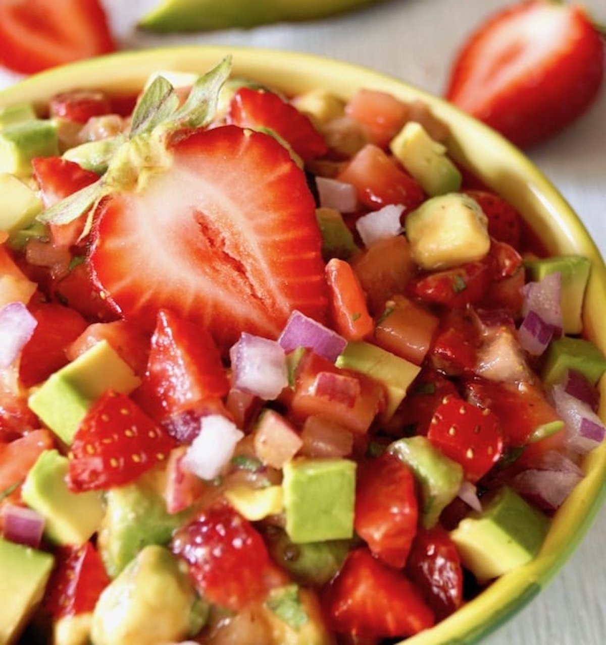 Light green bowl filled with strawberry and avocado salsa, with a halved strawberry on top.
