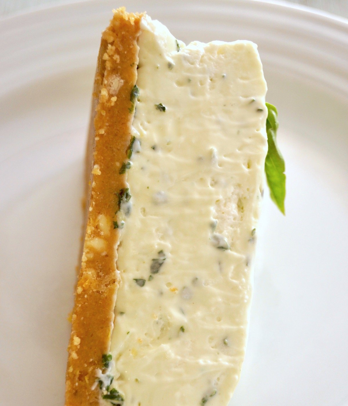 One slice of a basil cheesecake with a small basil sprig on its side on a white plate.