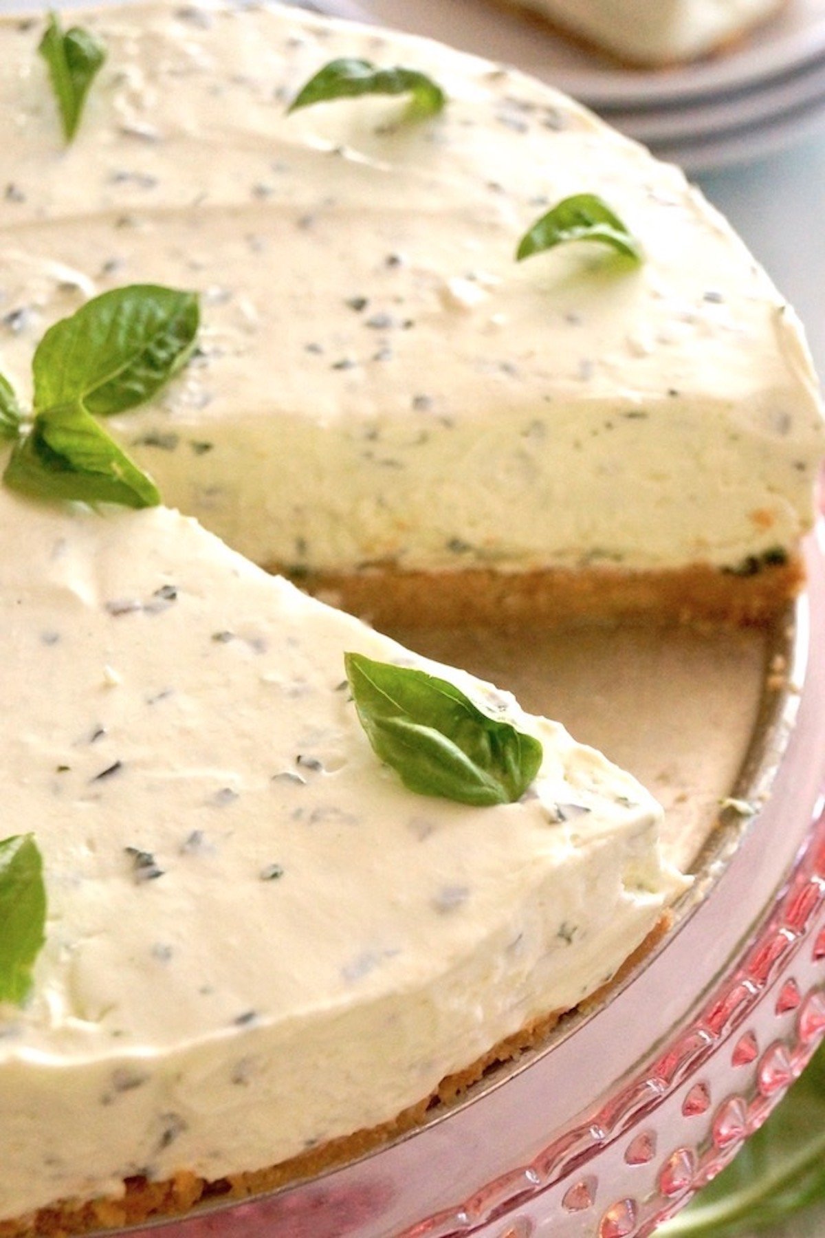 Top view, close up of a Basil Cheesecake with one slice removed and many small basil leaves on top.