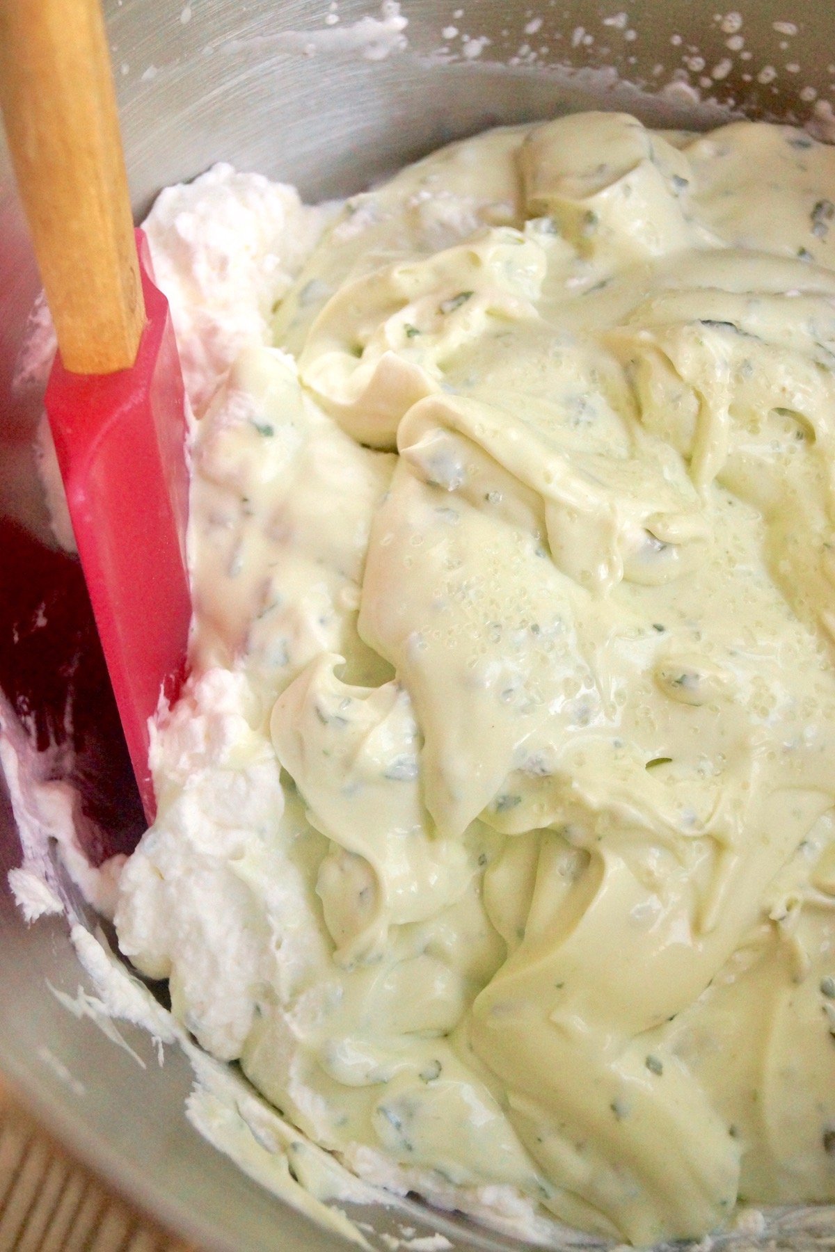Bowl with pink rubber spatula folding basil cream cheese mixture into whipped cream.
