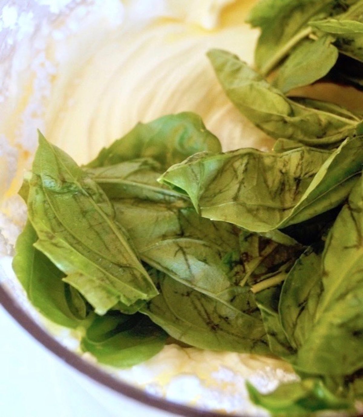 Cream cheese and fresh basil leaves in a food processor bowl.