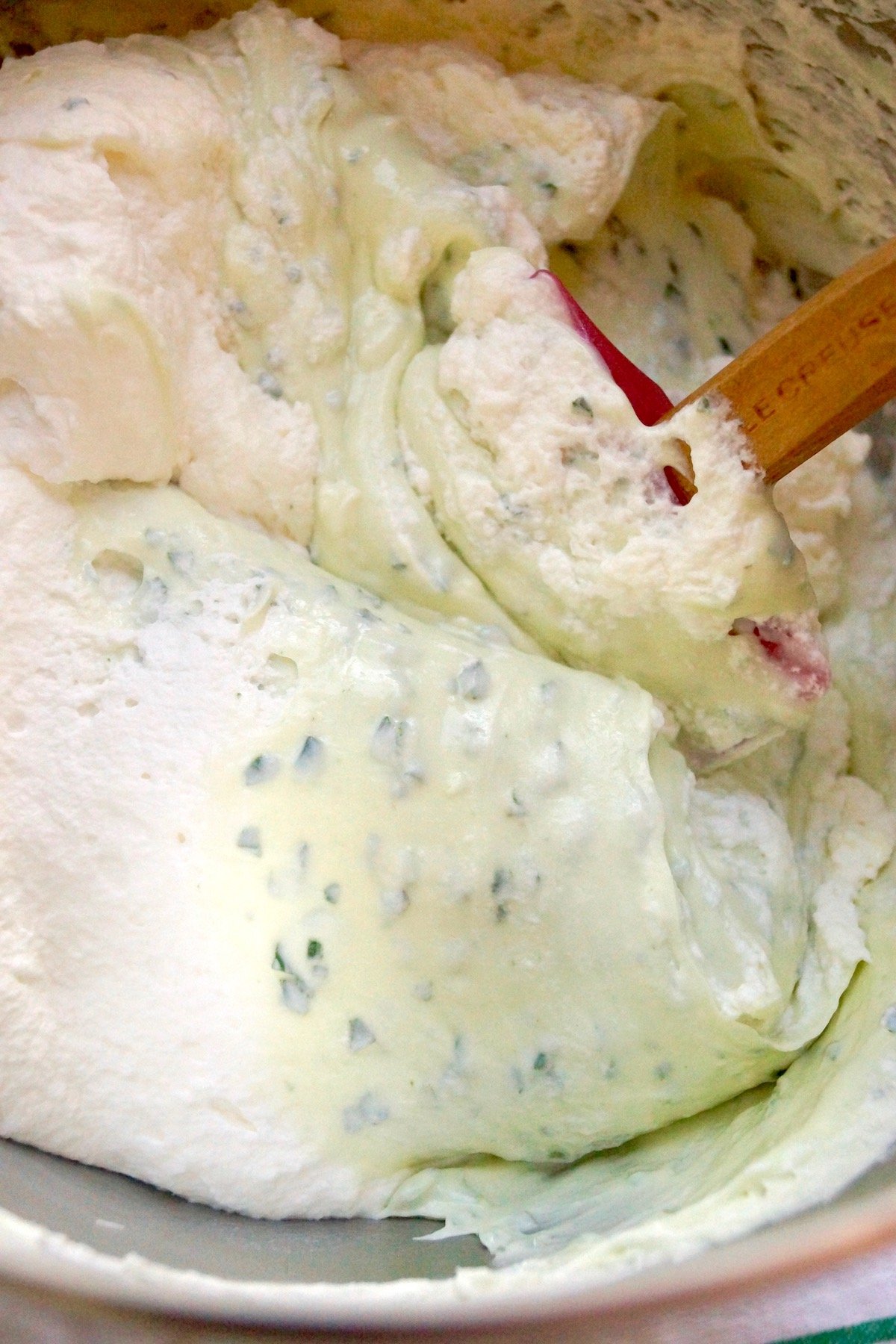 Top view of folding basil cream cheese mixture into whipped cream.