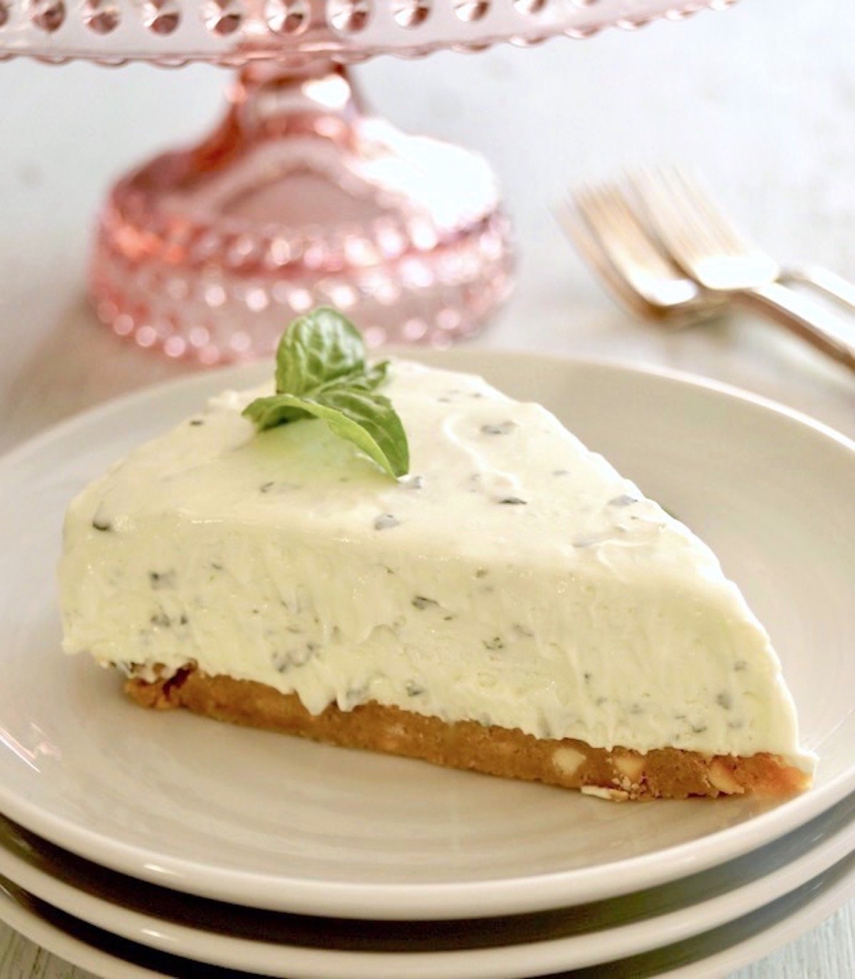 One slice of a basil cheesecake with a small basil sprig on top, on a white plate.