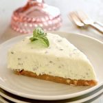 One slice of a basil cheesecake with a small basil sprig on top, on a white plate.